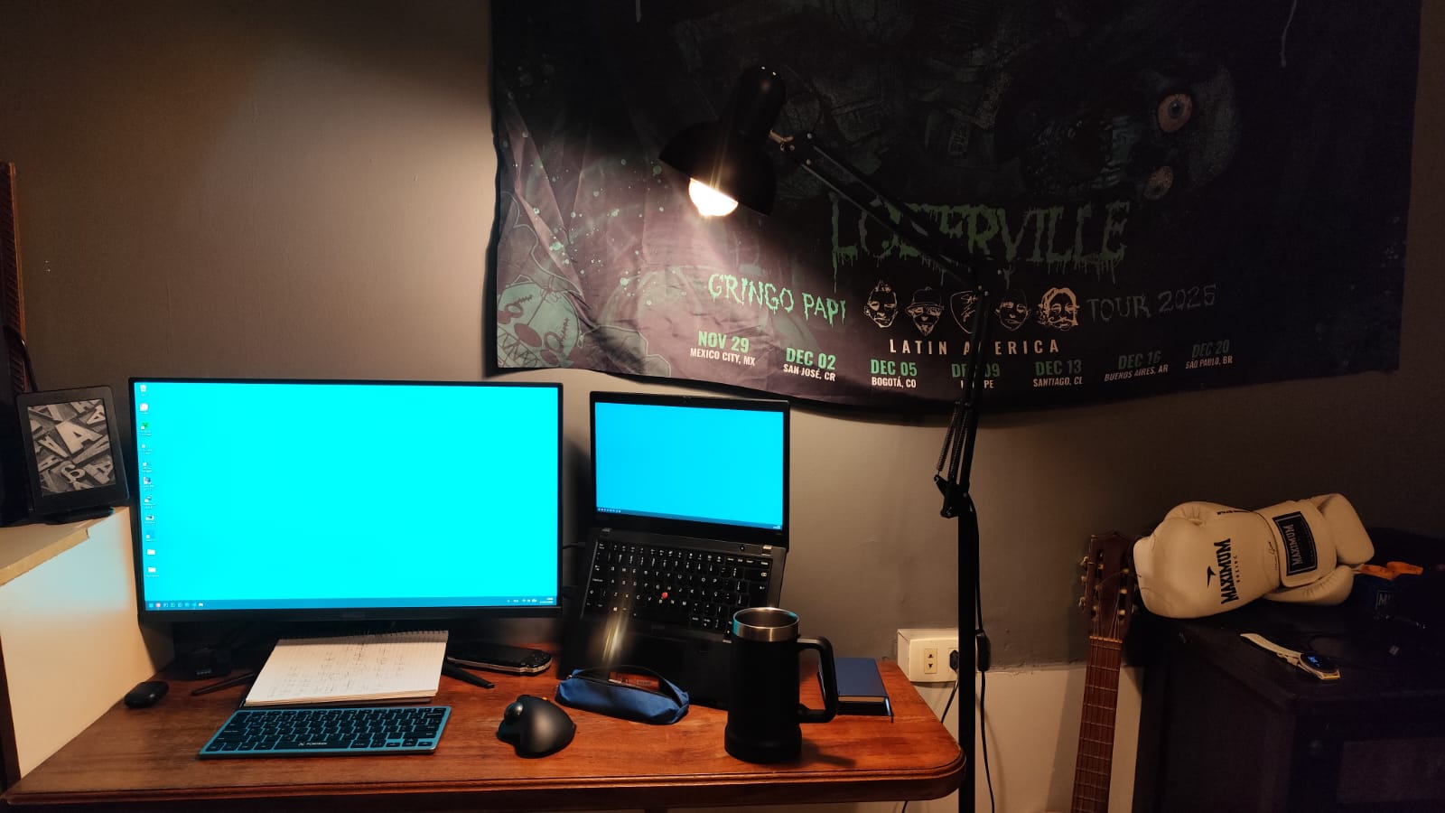 A computer Desktop with a monitor and a notebok on the left, a lamp on the middle and a guitar and boxing gloves on the right